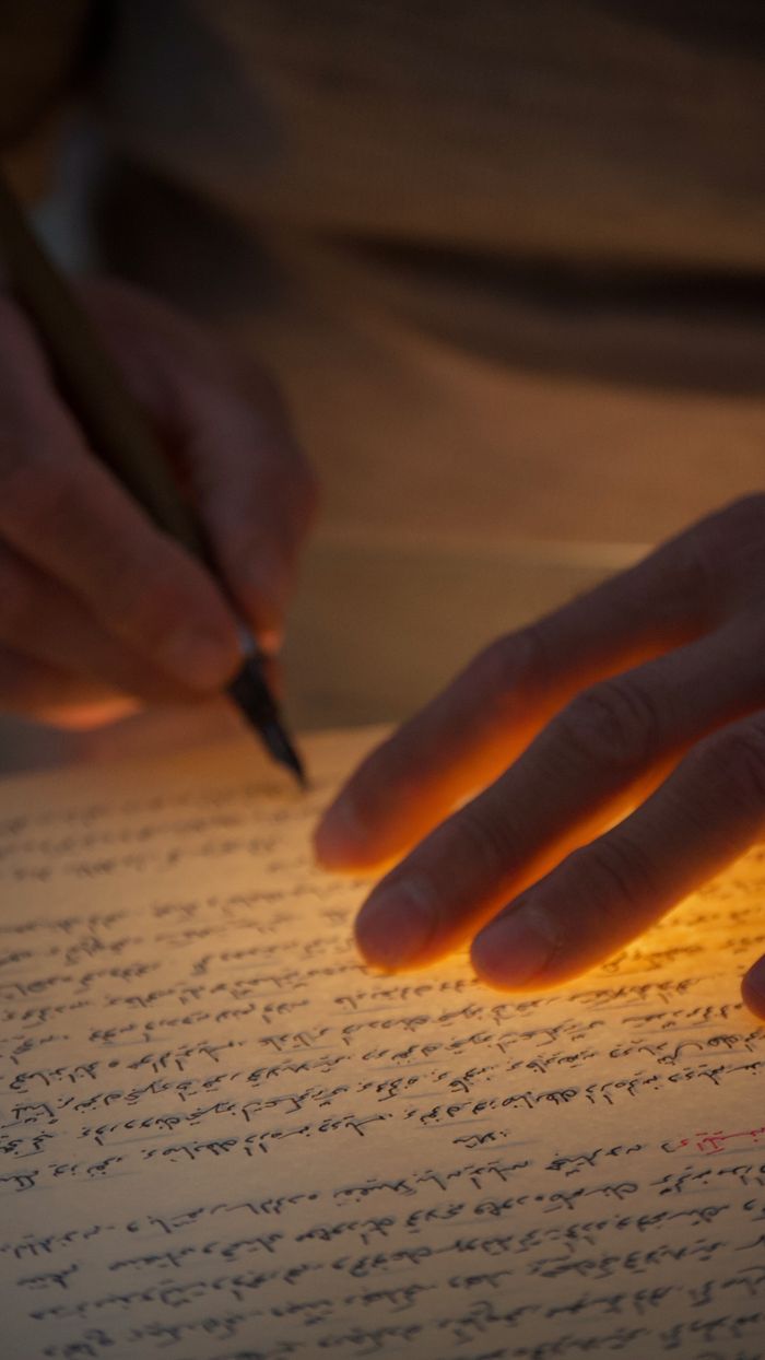 A hand writing on illuminated paper with warm, dramatic lighting effects.