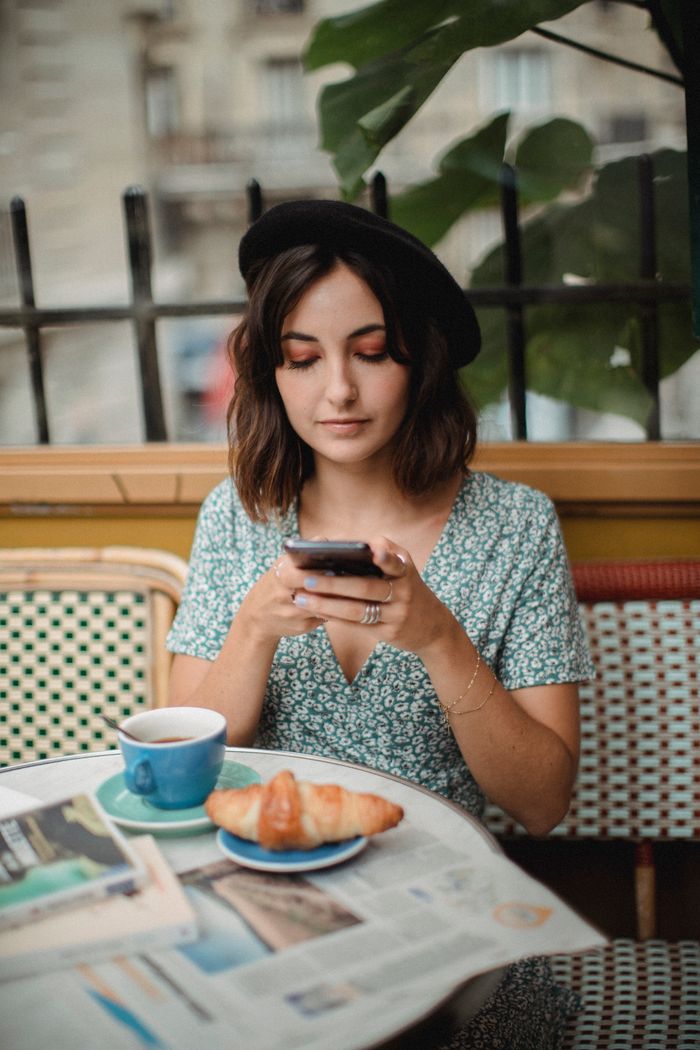 A woman sips coffee and checks her phone at a charming cafe with a croissant.